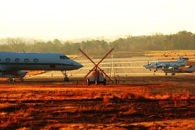 Airplane on airport runway against sky during sunset