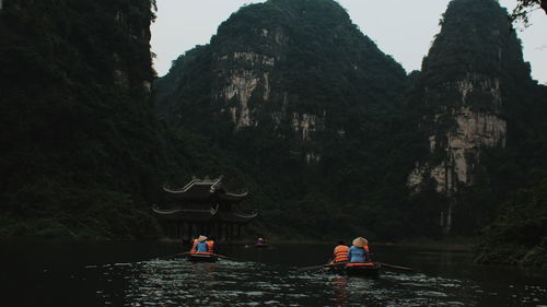 Rear view of people on boat in river against mountains