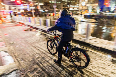 Rear view of person riding bicycle on city street