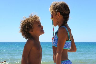 Close-up of siblings at beach against clear sky