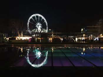 Illuminated ferris wheel by river in city at night