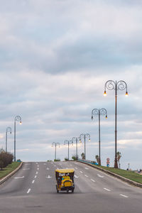 Vehicles on road against cloudy sky