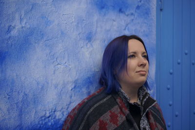 Young woman looking away against blue wall