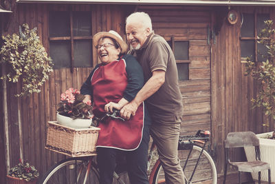 Happy senior couple riding bicycle by house