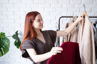 Beautiful young woman in trendy outfit standing in front of hanger rack and choosing outfit dressin