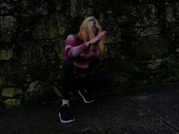 Full length of young woman crouching against weathered wall