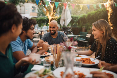 Smiling young man and women listening to male friend talking during dinner party in backyard