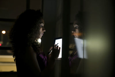 Businesswoman standing by whiteboard using tablet computer in dark office