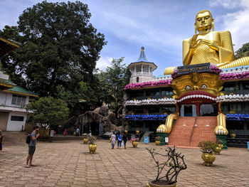 Statue amidst trees and buildings against sky