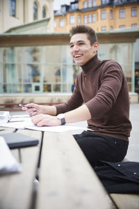 Smiling teenage boy looking away while sitting at table in schoolyard