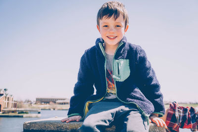 Portrait of smiling cute boy sitting against clear sky