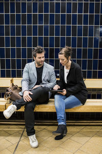 Full length of business people discussing over digital tablet while sitting on bench at subway station