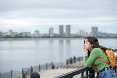 Portrait of young woman standing against river