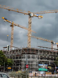 Cranes on construction site against cloudy sky