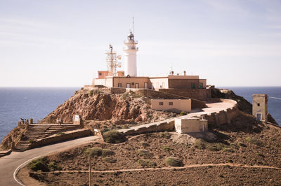 Lighthouse amidst buildings by sea against sky