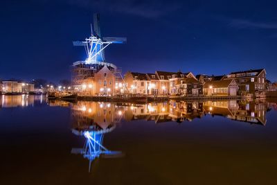 Reflection of illuminated traditional windmill and houses on calm lake at night
