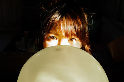 Portrait of young woman with balloon against black background