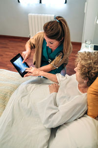 Woman holding mobile phone while sitting on bed at home