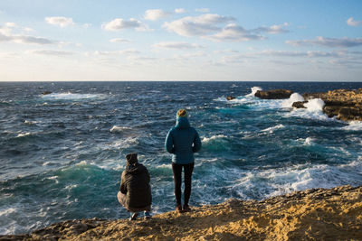 Rear view of friends at beach against sea during sunset