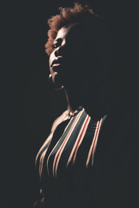 Side view silhouette of african american female with frizzy hair standing in darkness on black background