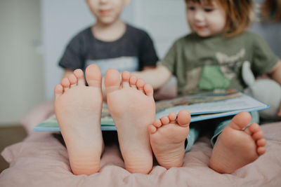 Big brother and little sister holding bare feet close up to camera . blurred face on background . 