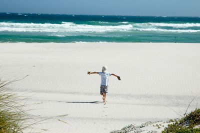 Rear view of man with arms outstretched walking at beach