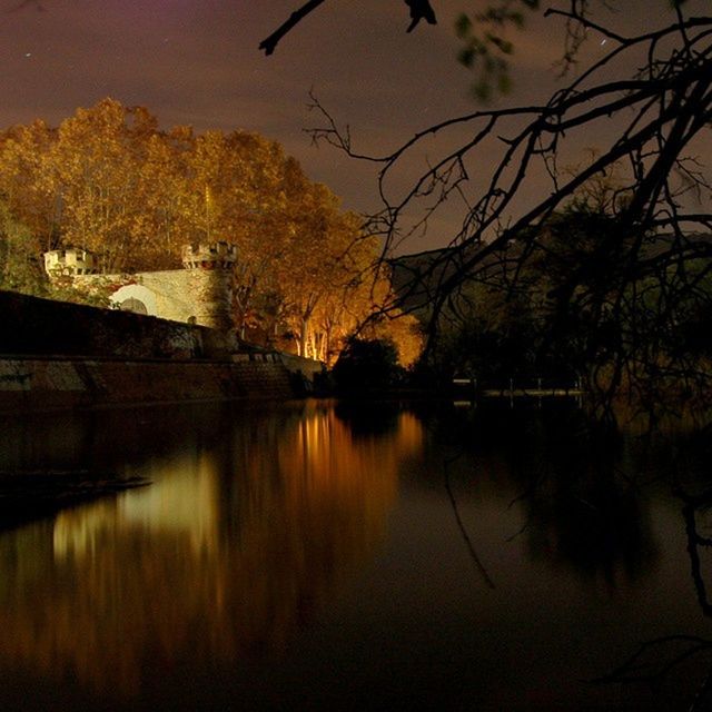 reflection, water, tree, lake, waterfront, built structure, architecture, tranquility, sunset, bare tree, standing water, river, tranquil scene, building exterior, nature, scenics, sky, beauty in nature, branch, outdoors