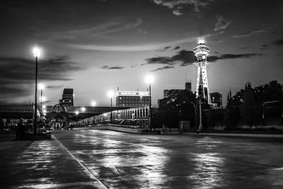 Illuminated street amidst buildings against sky at night