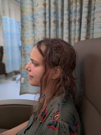 Side view of young woman looking away while sitting on chair at home