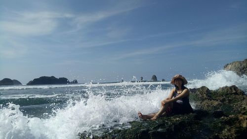 Man sitting on rock at sea against sky