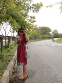 Side view of woman wearing sunglasses standing on road against sky