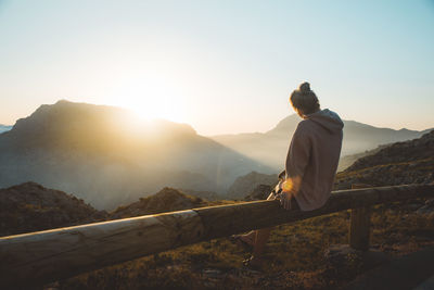 Rear view of young woman looking at mountains while sitting on railing