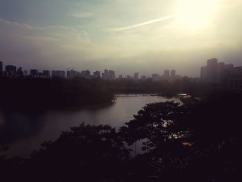 Silhouette buildings by river against sky in city