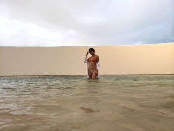 Portrait of bikini woman standing in sea against sky