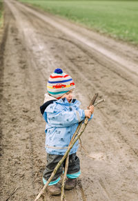 Full length of girl wearing knit hat holding stick on dirt road