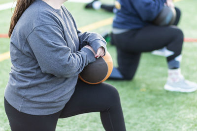 Female high school track and field thrower resting on one knee holding a medicine ball.