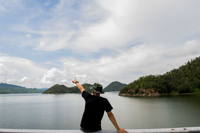 Man pointing at lakeshore against cloudy sky