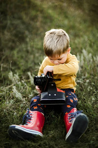 Boy with camera while sitting on grassy field