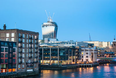 Buildings by river against clear blue sky