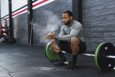 Athlete dusting chalk powder sitting on barbell in gym