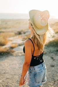 Woman wearing hat while standing at beach during sunset