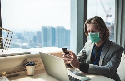 Man using mobile phone over laptop on table