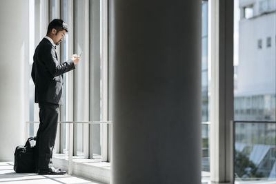 Side view of businessman using smart phone while standing by window in office