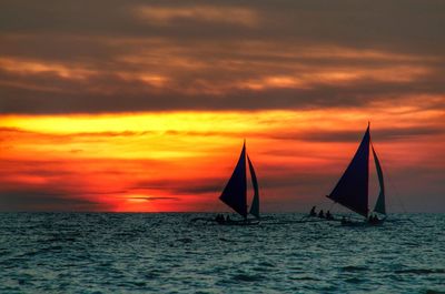 Sailboats on sea against cloudy orange sky