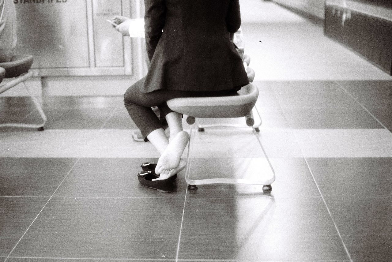 LOW SECTION OF WOMAN SITTING ON SEAT IN TILED FLOOR