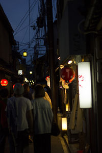 Rear view of people walking on illuminated street at night