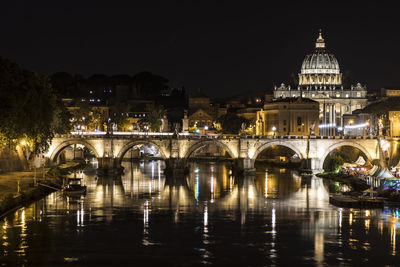 Illuminated bridge over river against buildings in city at night