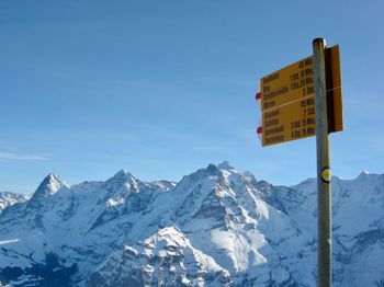 Information sign on snowcapped mountains against sky