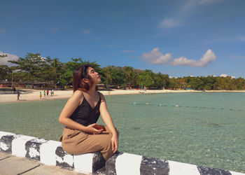 Young woman sitting on beach against sky