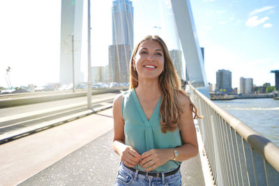 Confident young smiling woman walking on erasmus bridge at sunset in rotterdam, netherlands